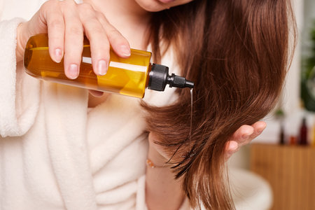 Woman applying oil on her long shiny hair against bathroom background, hair health careの写真素材