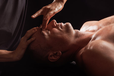 girl masseur doing facial massage to man on dark background close-up, facial skin rejuvenation, relaxation and meditationの写真素材