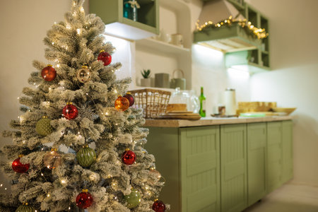 A cozy, bright kitchen decorated for Christmas with green cabinets, a small Christmas tree with decorations, and a festive table with snacks.の写真素材