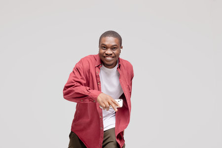 young African American man pictured isolated on gray background wearing casual clothes and hat dancing to music he is listening through wireless earphones, feeling relaxed and happyの写真素材