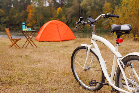 orange tent set up on grassy lake shore, bicycle in front of it, bicycle tourism, green tourism conceptの写真素材