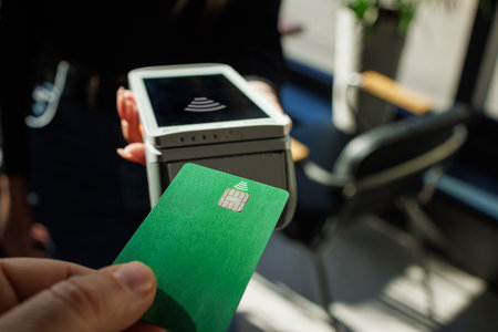 Close Up of a Masculine Hand Holding a Credit Card with an NFC Payment Technology Used for Paying. Customer Uses Debit Card to Pay Through Bank Terminal.の写真素材