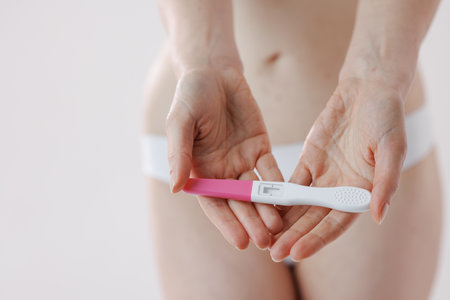 A woman shows a pregnancy test against her body in a bright bathroom, showing anticipation and uncertainty about the resultsの写真素材