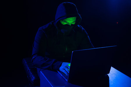 Hackers wear hoods to cover their faces. Hacking to steal important information. Use a computer to release malware viruses Ransom and harass organizations. He sitting in the dark room with neon lightの写真素材