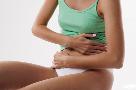 Young woman in white underwear touching left side of stomach suffering from severe abdominal pain, white background, cropped, close-upの写真素材