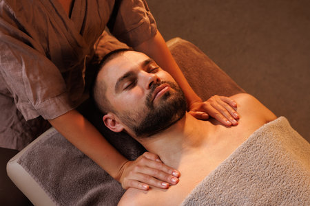 girl masseuse massages man's chest in warm atmosphere of spa salon, relaxing wellness massage for patientの写真素材