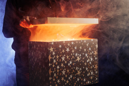 human hands taking out surprise from mysterious box on dark red background surrounded by smoke, mystery boxの写真素材