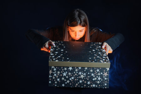 A young girl opens a mysterious gift box surrounded by smoke and blue light, creating a magical atmosphere.の写真素材