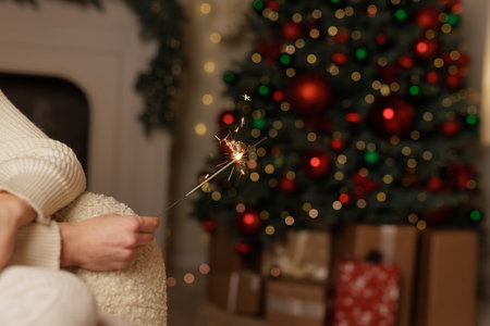 female hand holding sparklers against christmas tree background close up, merry christmas.の写真素材