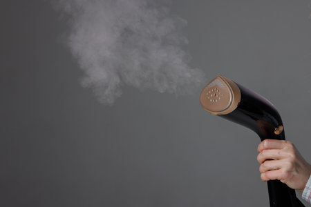 handheld steamer in womans hand with steam on grey background, close up.の写真素材