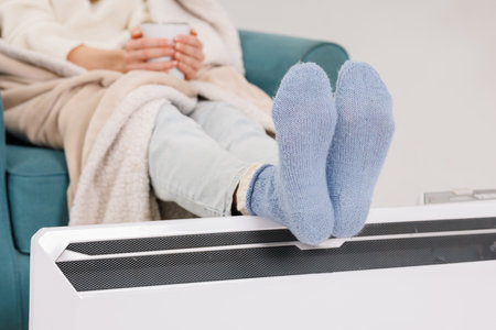 Young girl in warm knitted socks warms her feet on a radiator. Heating season concept.の写真素材