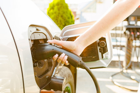 An electric vehicle charging at a station, with a close-up of the charging port. In the background,...