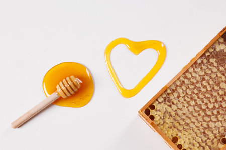 spoon with spilled honey and bee honeycomb on white background, top view, beekeeping concept
