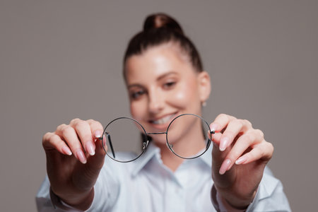 Smiling woman holding round eyeglasses in front of her, offering a clear vision concept, close-up shot.の写真素材