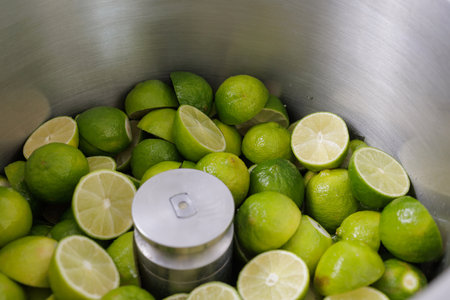Fresh limes being processed in an industrial stainless steel juicer for citrus juice extraction.の写真素材