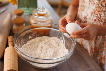 Child holding egg over bowl of flour preparing to bake, cozy kitchen scene with baking tools and...