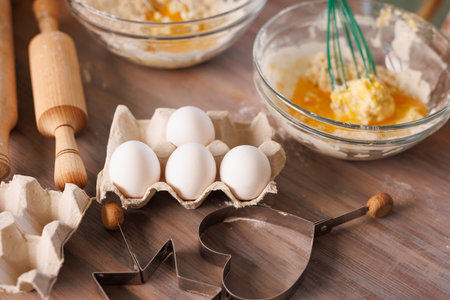 Children whisking flour and eggs in glass bowls while baking cookies together in a warm, rustic kitchen setting.の写真素材