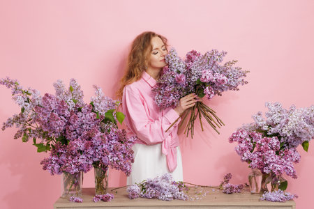 Woman enjoying the scent of fresh lilac flowers in bouquet arrangement on pink background, spring floral mood.の写真素材