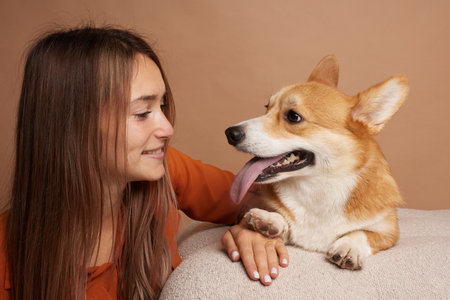 Happy woman smiling at her playful Corgi dog with tongue out, enjoying bonding time together indoors.の写真素材