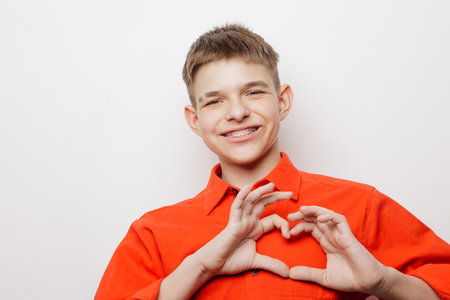Smiling teenage boy with braces making a heart shape with hands, showing confidence and dental positivity.の写真素材
