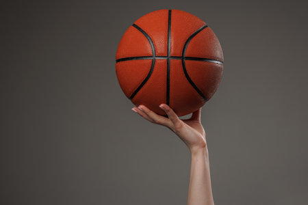 Female hand holding basketball up in the air on dark background, symbolizing power, focus, and athletic ambition.の写真素材