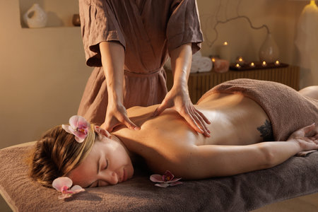 Woman receives professional back massage at peaceful spa with flowers and candles, promoting relaxation and wellness in tranquil environment.の写真素材