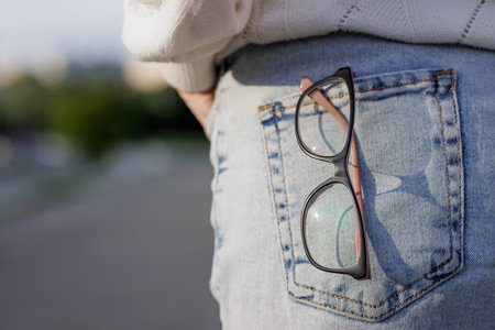 Eyeglasses in back pocket of jeans, captured in natural light. Everyday fashion, vision care, and casual street style concept.の写真素材