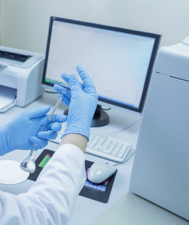 Lab technician in gloves analyzing samples with scientific glassware and computer in a modern...