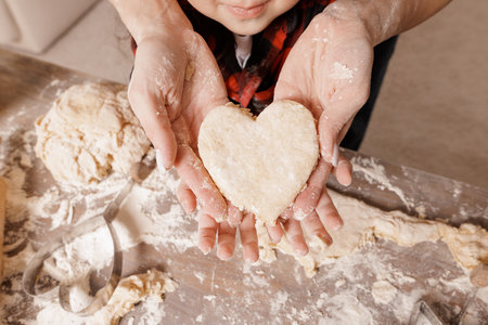 Close up of hands holding a heart shaped cookie dough, family baking together, symbolizing love, warmth, and home in the kitchen.の写真素材