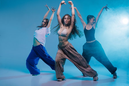 Group of young women dancing jazz funk with expressive moves in a modern studio filled with blue stage light and dynamic energyの写真素材