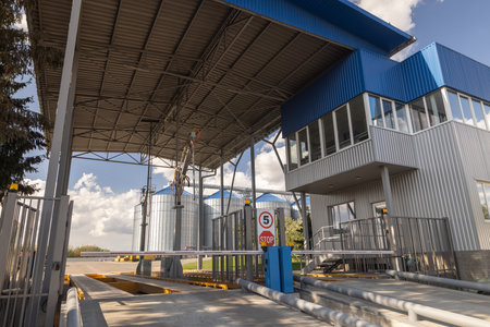 Industrial checkpoint entrance with modern security gate, office, and grain silos at logistics or...