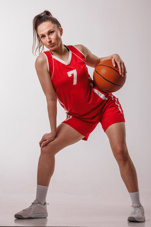 Confident young woman in red uniform posing with basketball, symbolizing athleticism, teamwork, and sports motivation.の写真素材