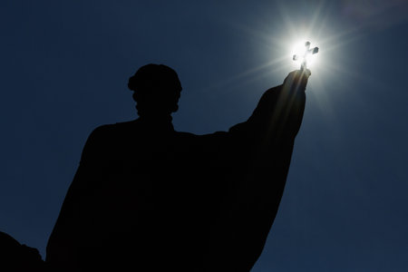 Dramatic silhouette of a person raising a cross towards the sun, symbolizing faith, hope, and spiritual inspirationの写真素材