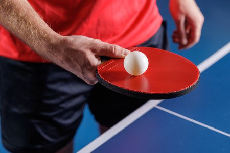 Closeup of player preparing a table tennis serve with red paddle and ball on a blue table indoor training and competition conceptの写真素材