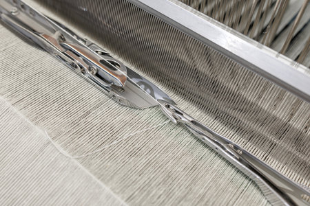 Close view of shuttle moving along reed on a modern loom with warp and weft in a textile factory...