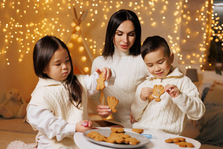 Mother and children decorate gingerbread cookies in a cozy room with glowing lights. Warm family holiday lifestyle ideal for seasonal projects.の写真素材