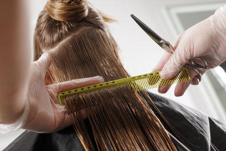 Gloved stylist sections and trims wet lengths with a comb and scissors, creating a clean straight...