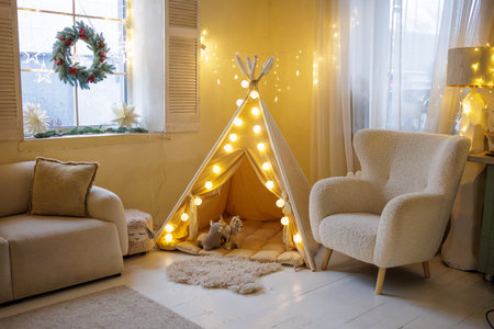 Warm Christmas kids playroom with glowing teepee tent, fairy lights and cozy Scandinavian decor for winter holidays at homeの写真素材