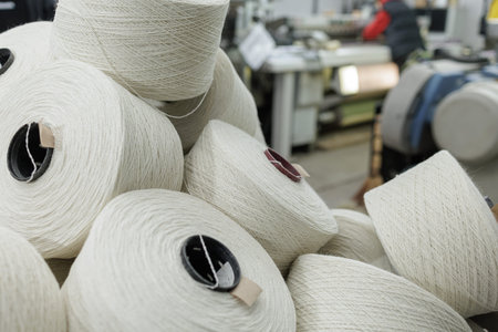 Stacked yarn cones near automated weaving equipment in textile factory, ideal for manufacturing,...