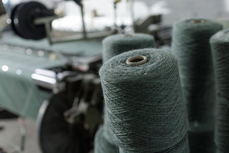 Closeup of yarn spools mounted on weaving machine in textile factory, ideal for manufacturing,...