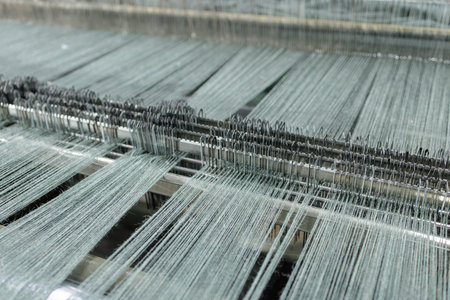 Warp threads aligned on automated weaving loom creating fabric, ideal for textile manufacturing,...