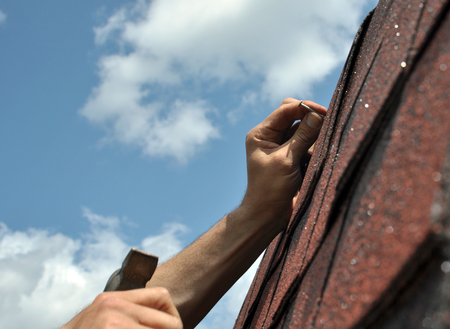 Hand with a hammer to drive a nail, roof repairsの写真素材