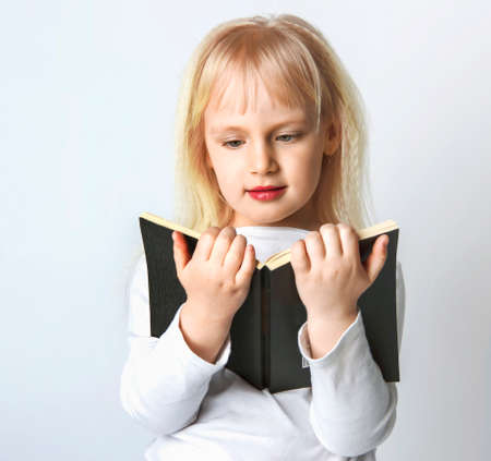 Portrait of cheerful smiling little schoolgirl girl with big book. The girl is learning to read. Back to schoolの写真素材