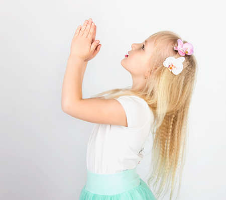 little blond girl folded her hands in prayer to God. A little angel. Side viewの写真素材