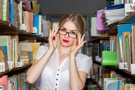 GIRL IN THE LIBRARY BETWEEN racks with books, a beautiful blonde with glasses gets knowledge and...