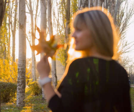 young woman girl with autumn yellow leaves in his hand an autumn leaf on a background of trees...