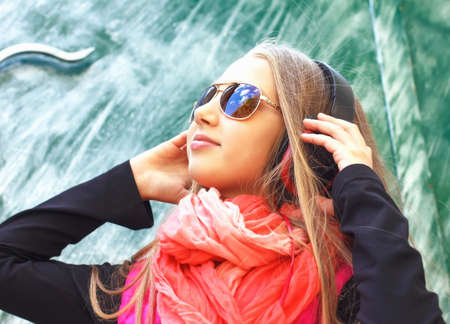 Urban fashionable girl posing outdoors in the city, listening to music on headphonesの写真素材