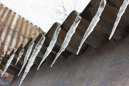icicles hanging from the roof on a background of cracked wall