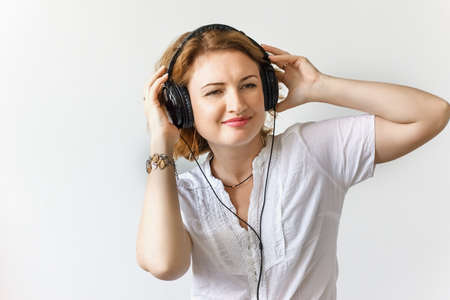 Beautiful girl with headphones listening to music and dancing in a white shirt, soft focus, studioの写真素材