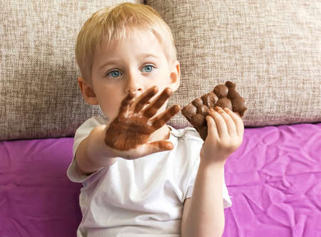 boy eating chocolate, holding a hand's candy, hands soiled in chocolate, pick up the child a chocolate, sweets harm teethの写真素材